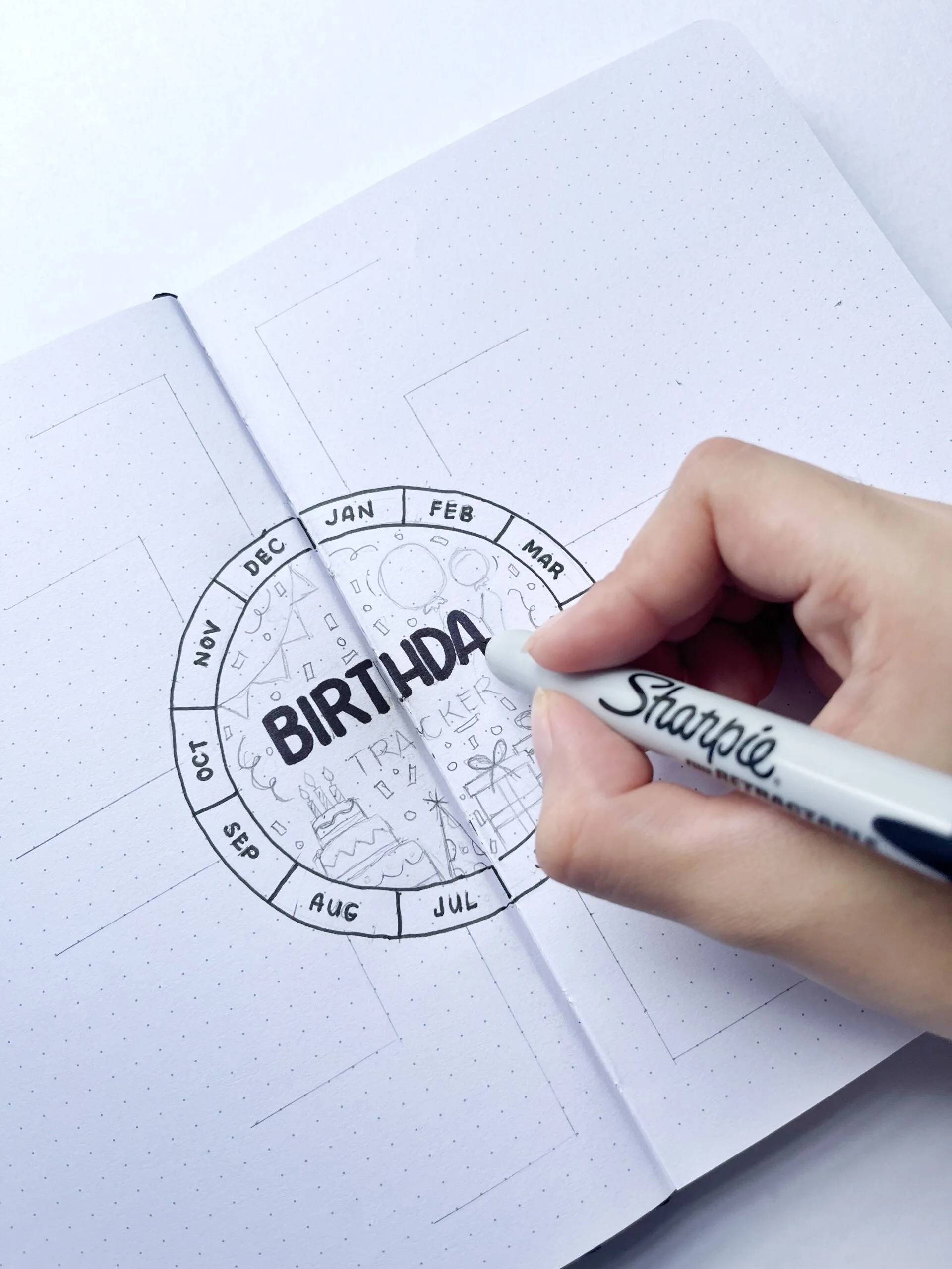A hand tracing the penciled outline of the birthday tracker layout with a pen.