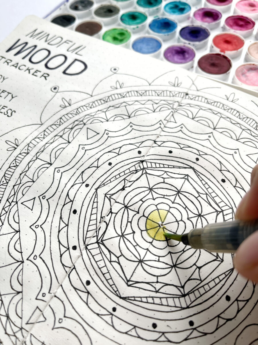Painting yellow paint on a bullet journal mandala.