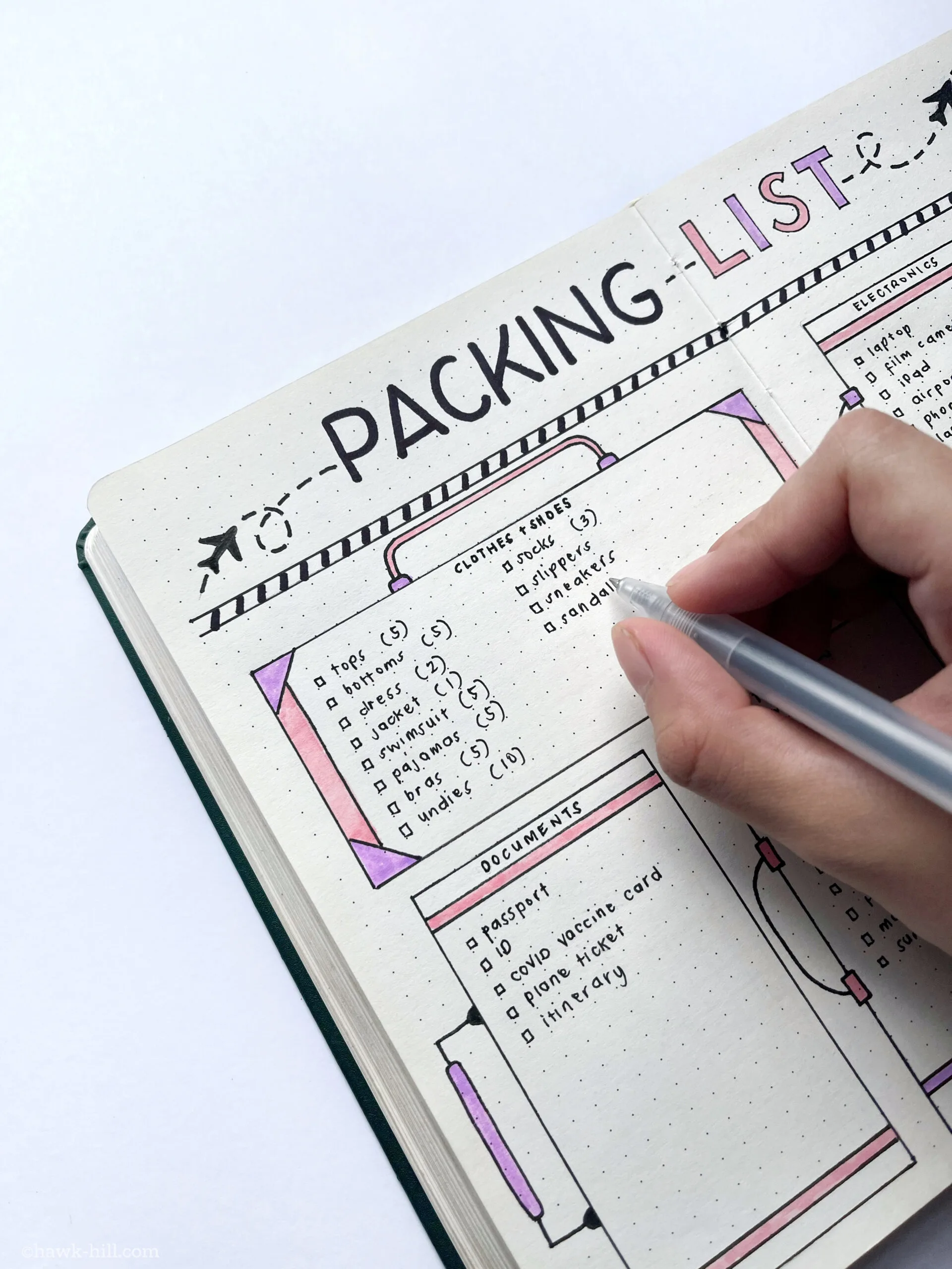 A hand fills out a bullet journal packing list for summer vacation.