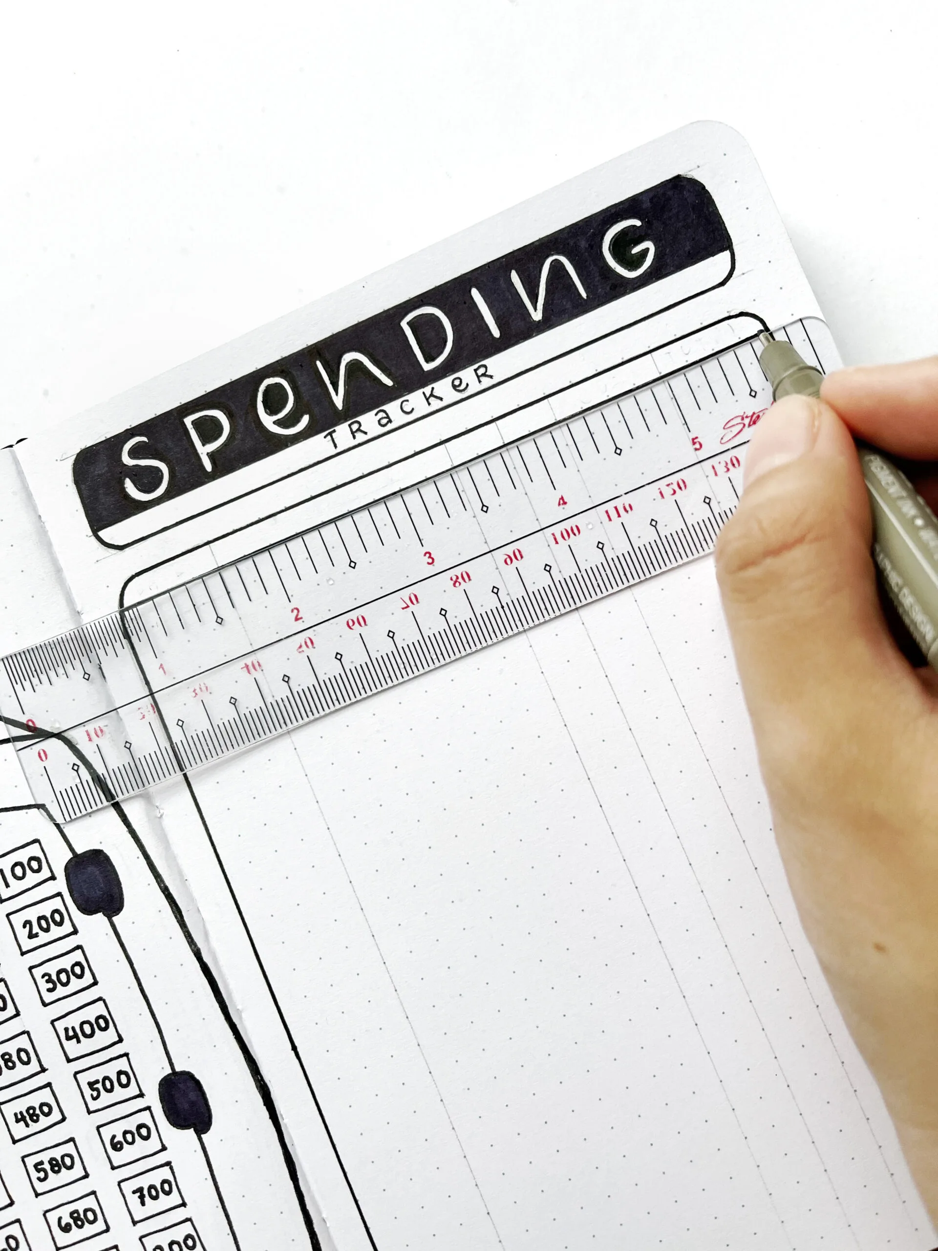 A hand tracing the spending tracker table with a pen in the bullet journal.