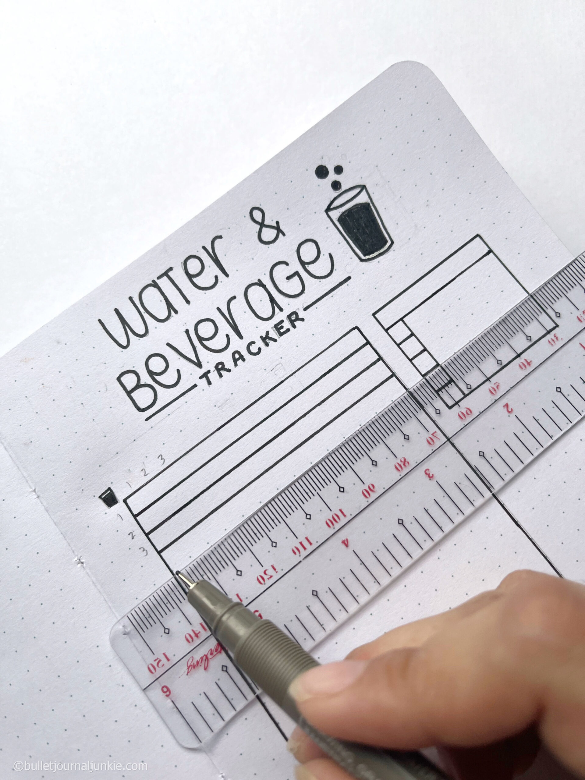 Using a ruler a hand draws a straight line on a water drinking tracker and a bullet journal.