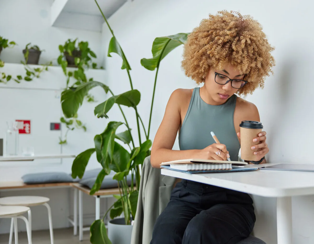 Woman journaling with a coffee cup in hand.