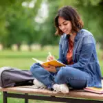 Woman sitting on a bench in the park and journaling.