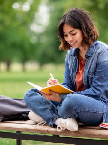 Woman sitting on a bench in the park and journaling.
