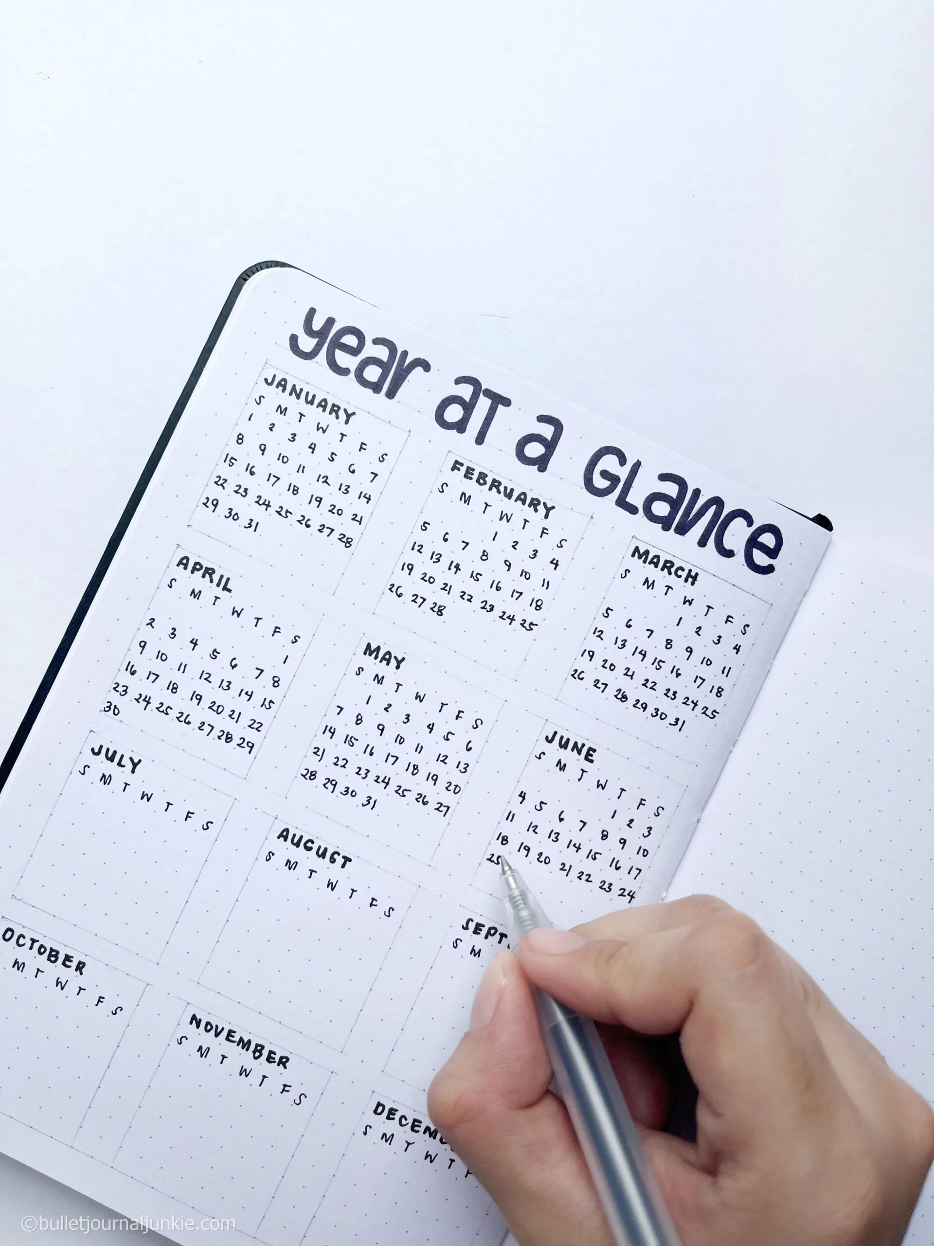 Writing the days of the month with a pen in the year at a glance bullet journal layout.